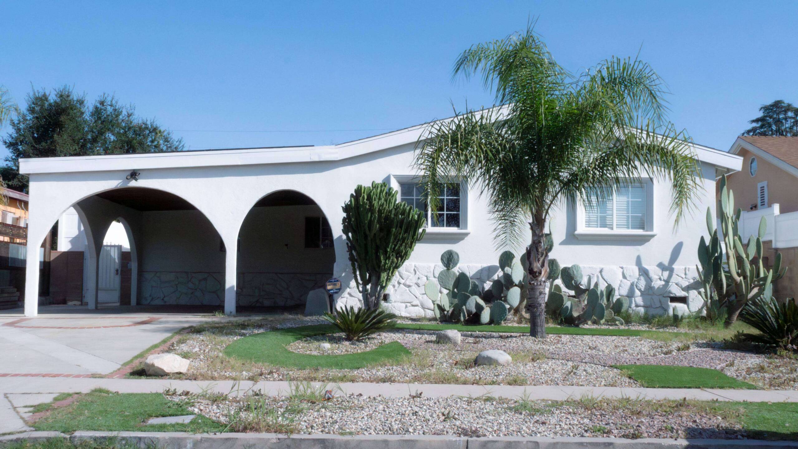 Center for Living residential housing facility exterior in California, featuring a white stucco building with a classic arched carport and low-maintenance desert landscaping.
